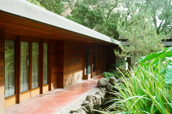 Wedding venue exterior with wood siding and glass doors, stone path and rock border leading past pond water and lush trees