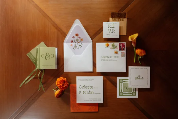 Invitation suite with wedding invitation suite cards, envelopes, vintage stamps, and a calla lily arranged on a wood tabletop flat lay
