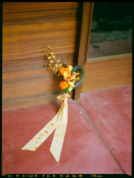 Bridal bouquet with orange wedding bouquet tones, calla lilies and long ribbon streamers, held against a wood wall by a window