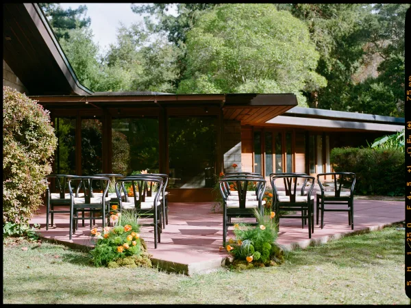 Ceremony setup with outdoor wedding ceremony seating, black chairs with white cushions and orange aisle flowers on a modern patio lawn