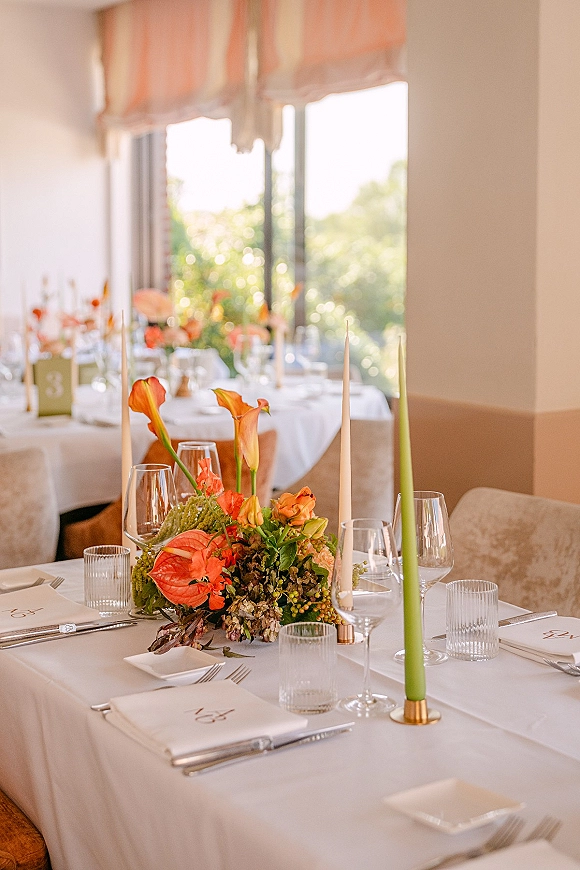 Reception tablescape with wedding table centerpiece of calla lilies and anthurium, plus green taper candles by windows and draped ceiling decor