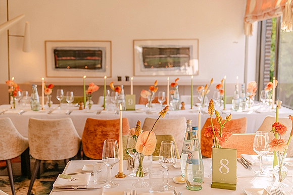 Reception tablescape with a modern wedding table setting on white linen, featuring taper candles, bud vases, place cards and glassware in an indoor dining room