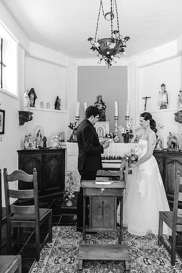 Wedding vows as the groom reads vows to the bride in a small chapel wedding, framed by altar candles and a crucifix behind them