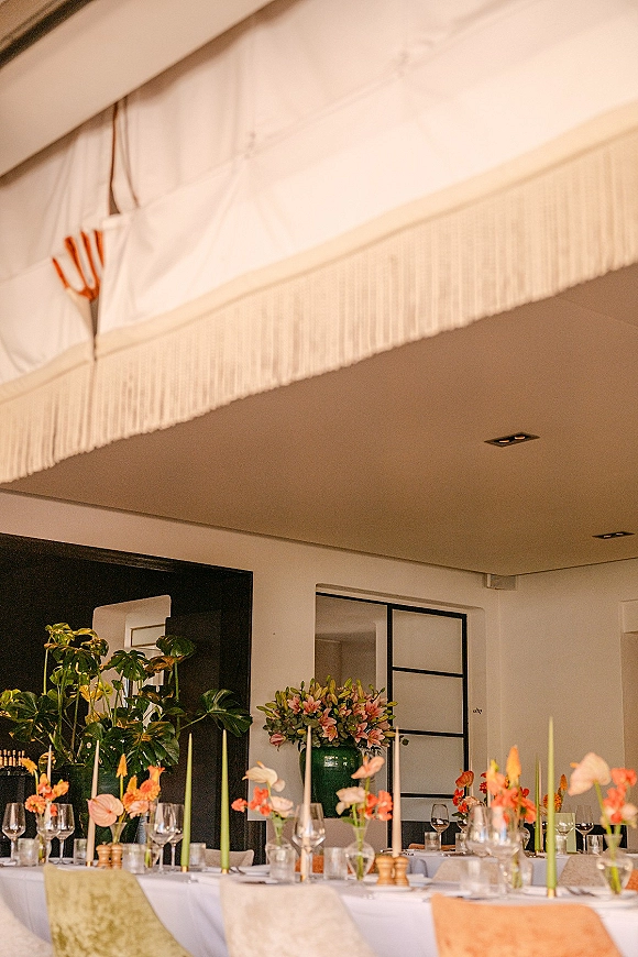 Reception tablescape with wedding table decor, green and white taper candles, anthurium centerpieces, and glassware in a bright indoor space