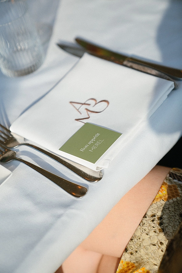 Wedding place setting with wedding napkin fold, place card on linen napkin, menu card, silver cutlery, and water glass in natural light shadows
