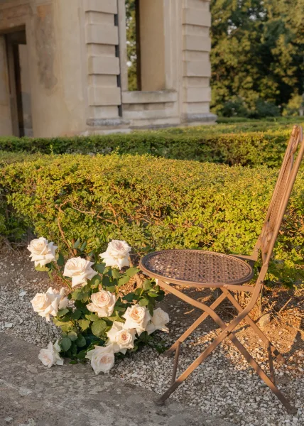 Garden wedding decor for a bistro chair wedding, set by a stone building with a gravel path and hedge in a leafy garden.