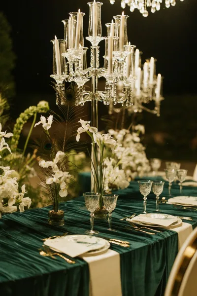 Reception tablescape with candelabra wedding centerpiece, taper candles and white florals on teal cloth, crystal stemware in a dim room with bokeh lights