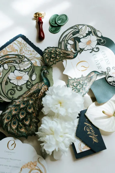Invitation suite featuring art nouveau wedding invitations with peacock motif, green wax seal and dark green envelope on a white surface
