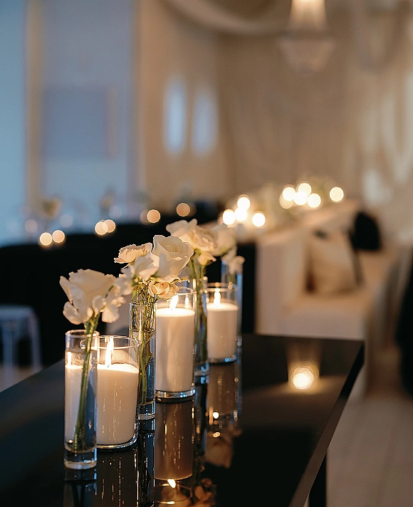 Wedding candle centerpiece with pillar and floating candles in clear cylinder vases, accented by white roses in a warmly lit reception room