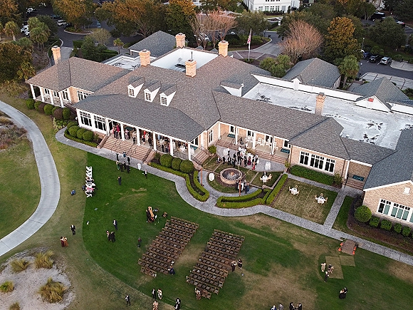 Outdoor wedding venue with aerial wedding venue view showing ceremony chair rows, string-lit patio, fire pit, and brick clubhouse porch on lawn