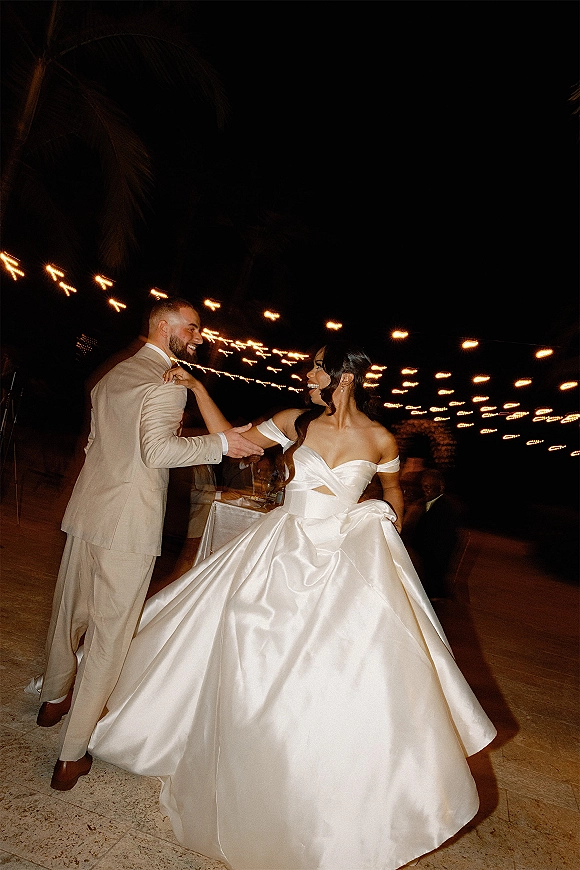 First dance on a wedding dance floor as the bride twirls her off-the-shoulder ball gown while the groom leads under string lights at night patio reception
