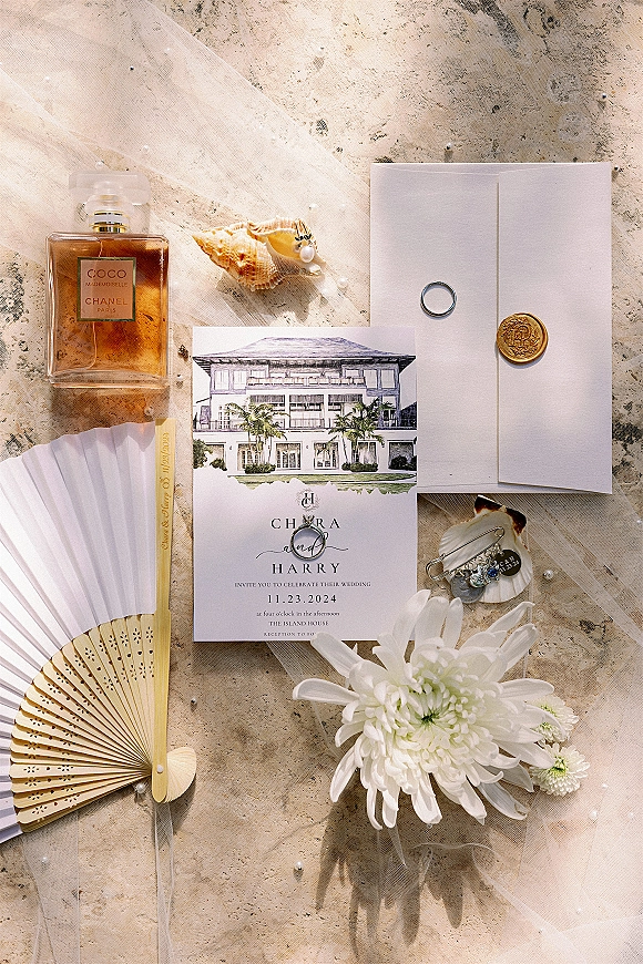 Invitation suite wedding invitation flat lay on stone surface with wax-seal envelope, rings, perfume, veil tulle, seashell, and pearl pins