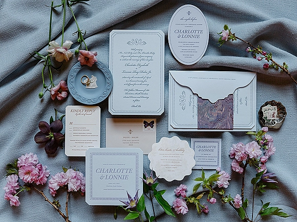 Invitation suite wedding invitation flatlay with RSVP and save the date, wax seal and ring, ribbon and blossoms on gray linen fabric