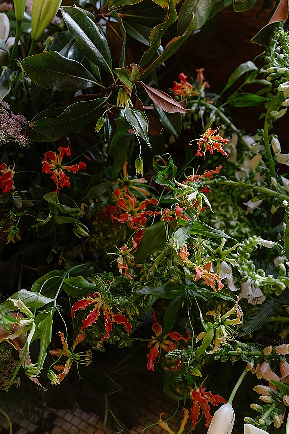 Wedding floral arrangement with tropical wedding flowers, orange and white blooms, and lush fern and magnolia foliage against a dark backdrop