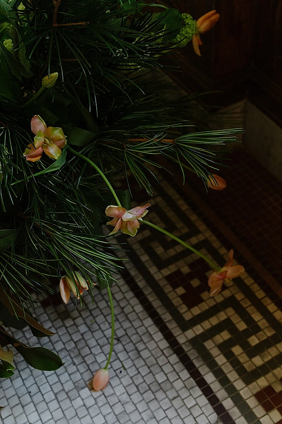 Wedding florals with bridal bouquet greenery, pine branches and small pink blooms arranged on a mosaic tile floor for a textural still life