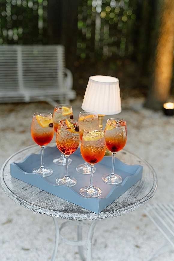 Wedding welcome drinks with signature wedding cocktails on a tray with citrus slices beside a lamp and candle on a garden patio bench