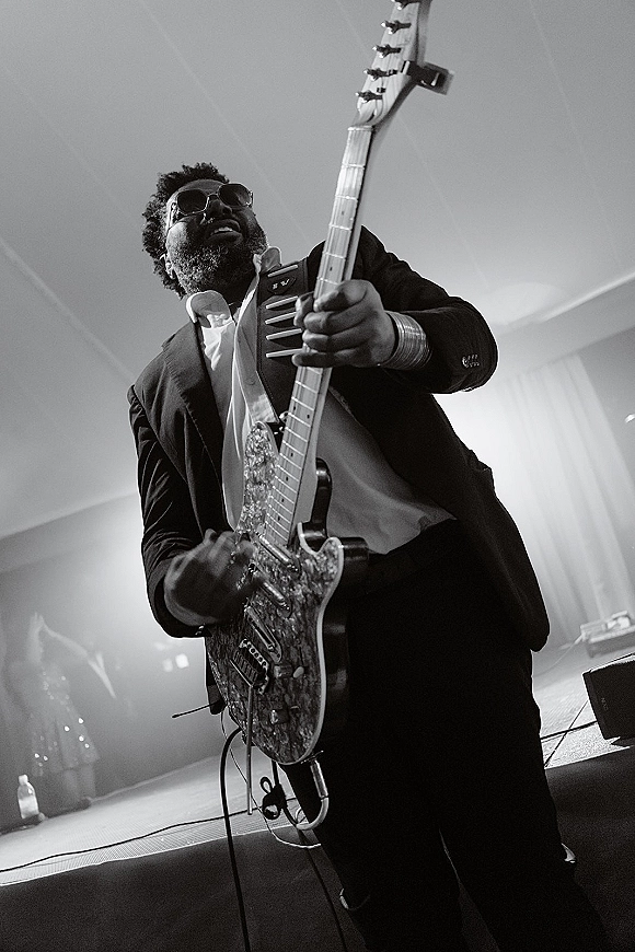 Wedding band performance with an electric guitar player in sunglasses at a hazy stage under concert lighting and draped ceiling, near cables