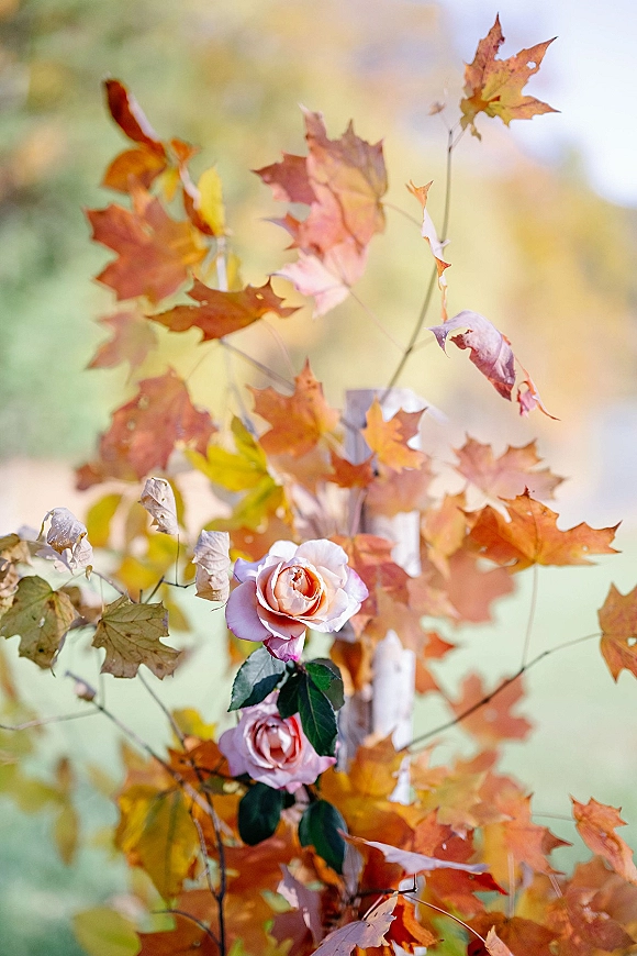 Fall wedding florals with autumn wedding flowers featuring peach roses, rust leaves, and branches, set against blurred outdoor greenery