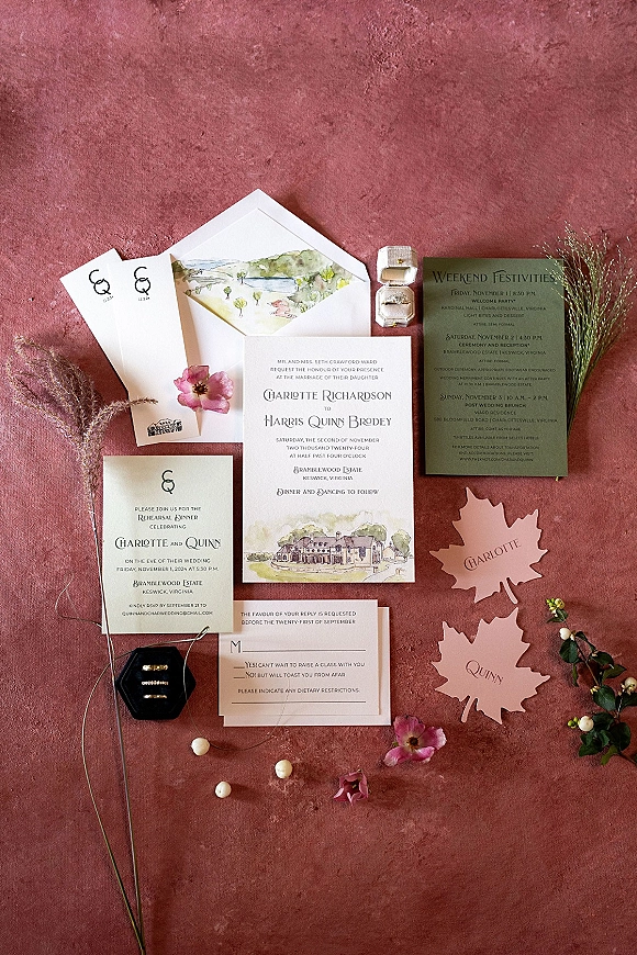 Wedding invitation suite with watercolor wedding invitations, envelopes, RSVP and venue illustration flat lay on rust velvet with ring box and dried florals