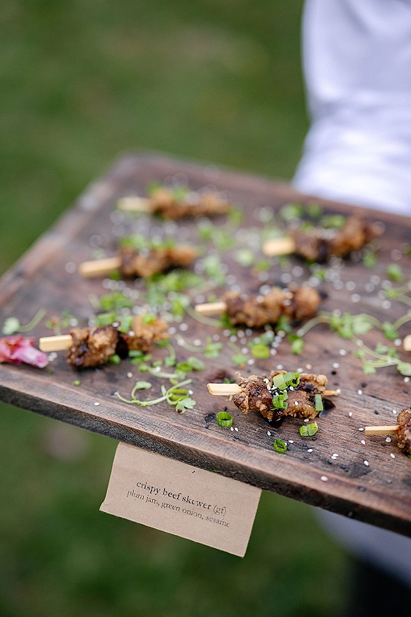 Wedding cocktail appetizers with passed hors d'oeuvres beef skewers on a wood serving board, sesame and microgreens, outdoors on a lawn