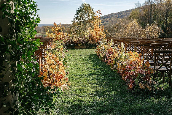 Ceremony aisle decor with floral lined ceremony aisle, cross-back chairs and roses with orange foliage on a lawn with mountain views