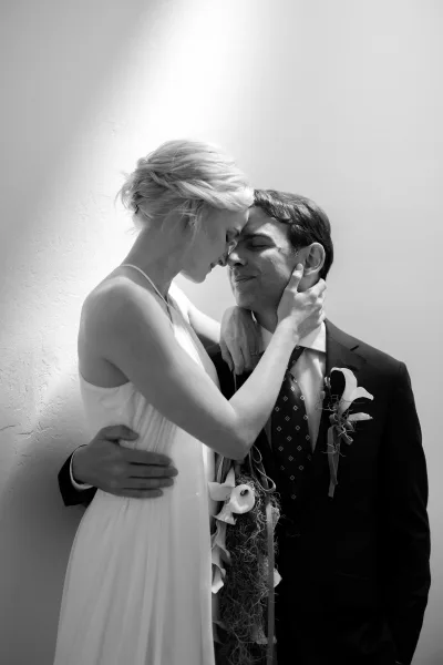 Couple portrait of a bride embracing groom, their foreheads touching as she holds a calla lily bouquet, captured in a tender, intimate moment.