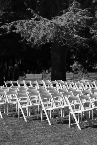 Ceremony seating arranged for outdoor wedding seating with folding chairs on a grass lawn, trees beyond and a lone park bench.