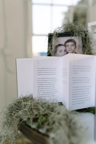 Vow book and accordion fold program arranged on a table beside a framed photo, presented together as a keepsake display.