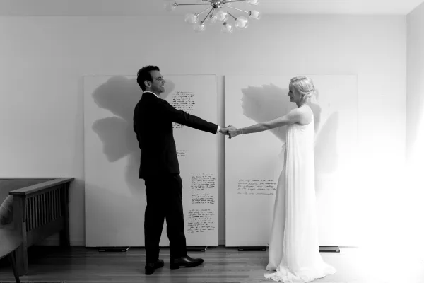 Couple portrait of a bride and groom holding hands, smiling softly against modern art panels in a relaxed, minimalist moment.