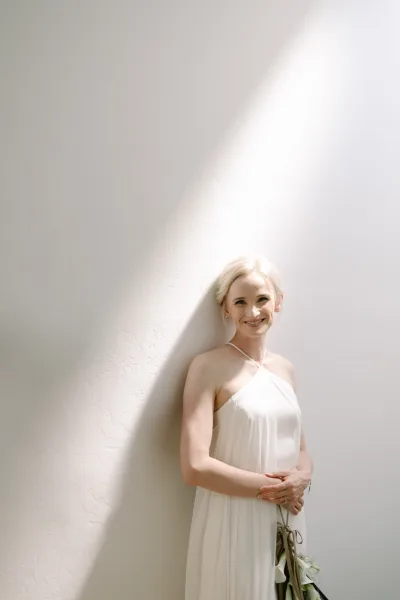 Bridal portrait of a bride holding a bouquet of white calla lilies, styled with a low bun in natural light for a clean, veil-free look