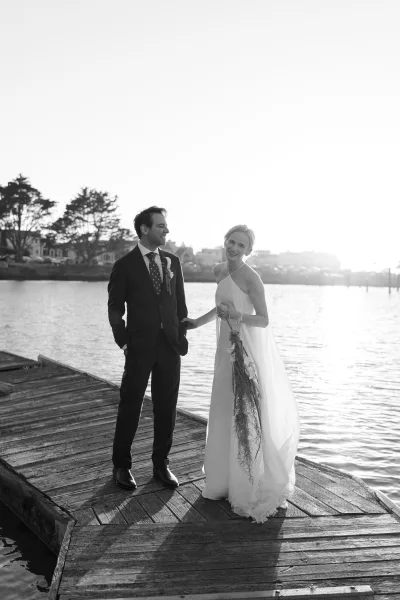 Couple portrait on a wooden dock, a waterfront wedding portrait as the bride holds a trailing bouquet beside her groom.