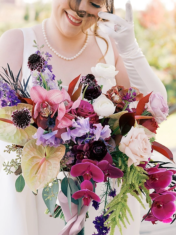 Bridal bouquet, colorful wedding bouquet of orchids, roses and anthurium with eucalyptus, held by a gloved bride in sunlit garden bokeh