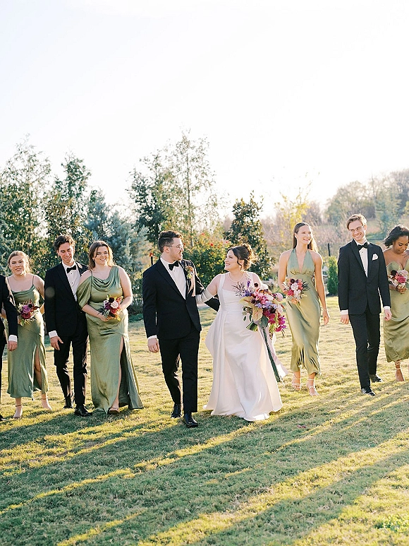 Wedding party portrait of the bride with bridesmaids and groomsmen, colorful bouquets and tuxedos, walking in a sunlit grassy field