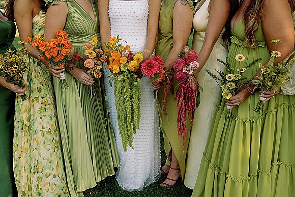 Bridesmaid bouquets of colorful bridesmaid bouquets with dahlias and zinnias held by women in mismatched dresses on a grass lawn outdoors