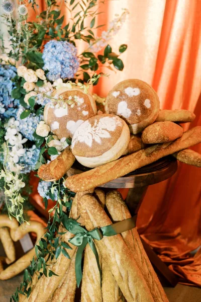 Hydrangeas and roses frame a bread display against a gathered backdrop of vivid orange drapery