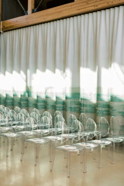 Clear acrylic chairs line the ceremony seating beneath green ombre drapery and exposed wood beams