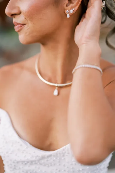 Gold teardrop earrings and a pendant necklace make up the bridal jewelry, shown against a beaded strapless bodice the bride touches.
