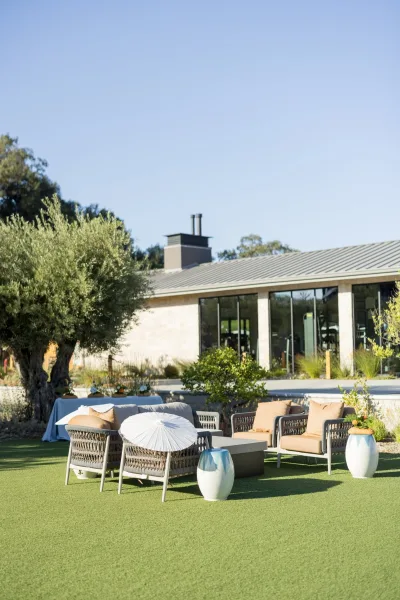 Woven chairs and blue-and-white cushions furnish an outdoor wedding lounge, with ceramic stools and a paper parasol nearby