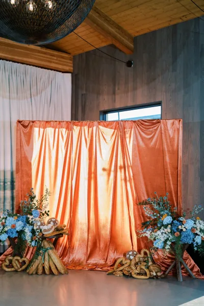 Copper satin drapery and blue-and-white hydrangeas frame a wedding backdrop, with greenery spilling around the display