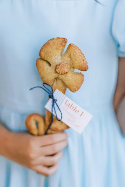 Bread on a wooden stick with a blue-striped paper tag tied in twine marks an edible escort card