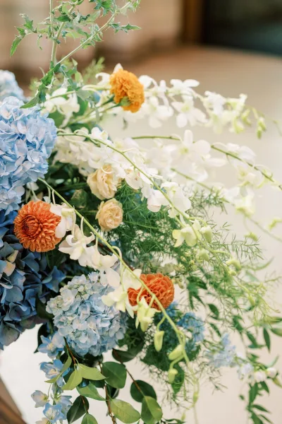 Blue hydrangeas and orange dahlias compose an asymmetrical wedding flower arrangement with a tall silhouette