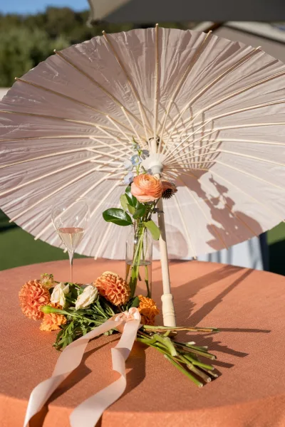 Peach linen and a paper parasol accent cocktail table decor at a leafy garden reception