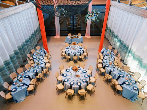 Blue linens and hanging florals add color and texture to the reception setup in a spacious room.