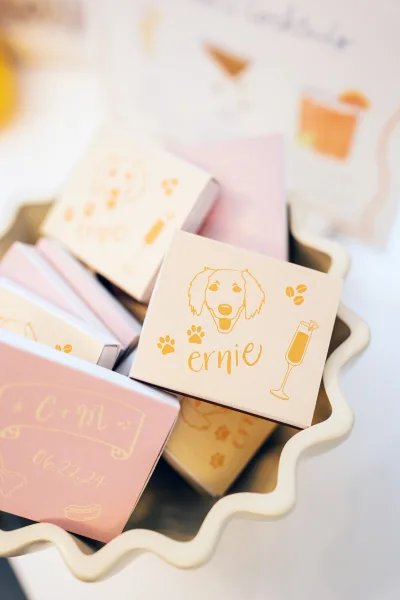 Wedding matchbooks and personalized matchboxes wedding favors in a scalloped ceramic bowl, blush pink with gold foil monogram on white tabletop