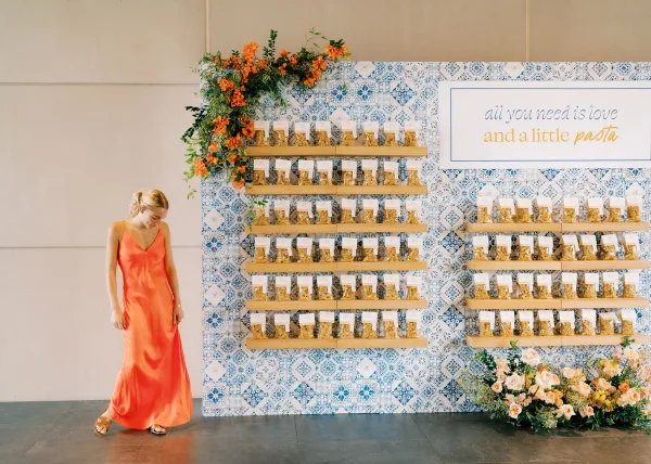 Wedding favor display with pasta wedding favors in bagged treats on shelving and escort cards, set against a blue patterned tile backdrop indoors
