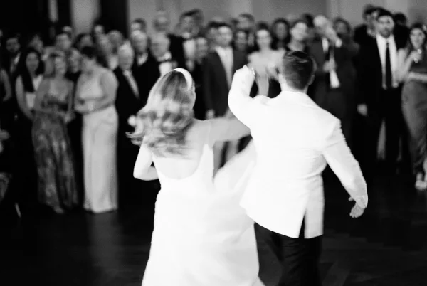 First dance as newlyweds twirl on the dance floor, bride in wedding dress and groom in suit jacket, with guests watching in the reception hall