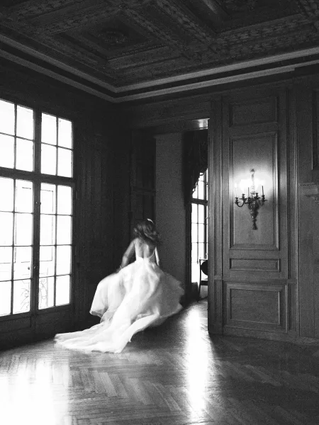Bridal portrait in a black and white wedding portrait style, bride twirling a long-train dress in a wood-paneled room by tall windows