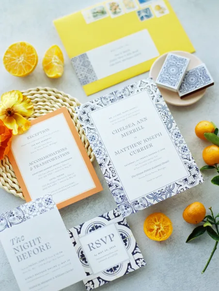 Wedding invitation suite with blue and white wedding invitations, RSVP and details cards, wax seals, stamps, citrus accents on stone surface