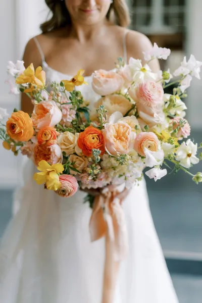 Bridal bouquet with peach wedding bouquet tones, garden roses and ranunculus with greenery, tied with ribbon in soft window light