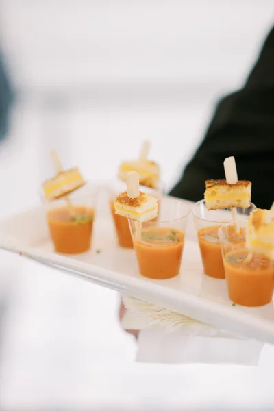 Wedding appetizers arranged on a passed tray with appetizer cups and mini grilled cheese bites on skewers against a white backdrop